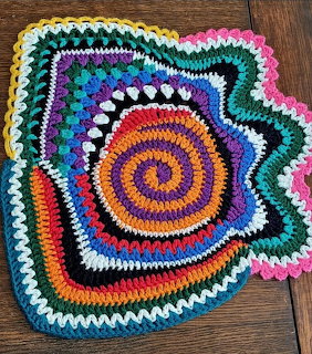Colorful spiral crochet mat with wavy edges on a wooden floor