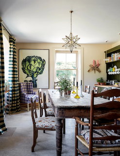 Warm dining room with dark wood table, patterned chairs, geometric light fixture, and large artichoke print