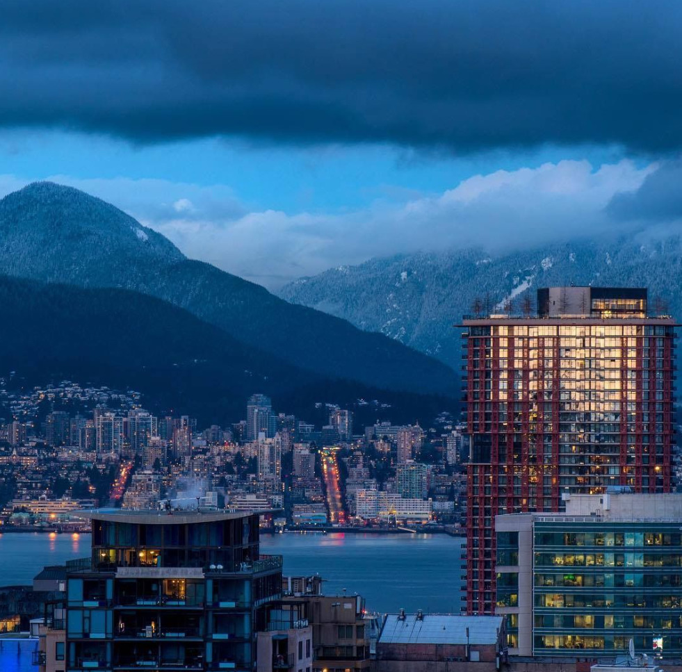 Vancouver skyline with tall buildings, water, mountains, and dark evening clouds