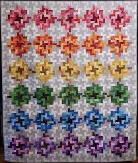 Patchwork quilt with rainbow-colored geometric flower blocks in rows against white fabric