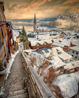 Snow-covered village of Hallstatt with church spire, lake, and mountains in winter