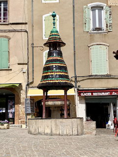 Tiered fountain in a cobblestone square with pastel buildings and shuttered windows