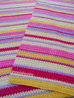 Folded crochet blanket with pink, yellow, purple and cream horizontal stripes