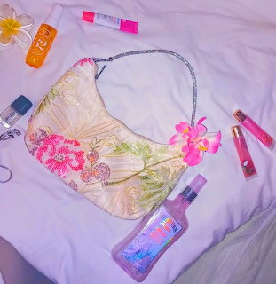 Tropical purse and beauty products arranged on white bedding with pink flowers