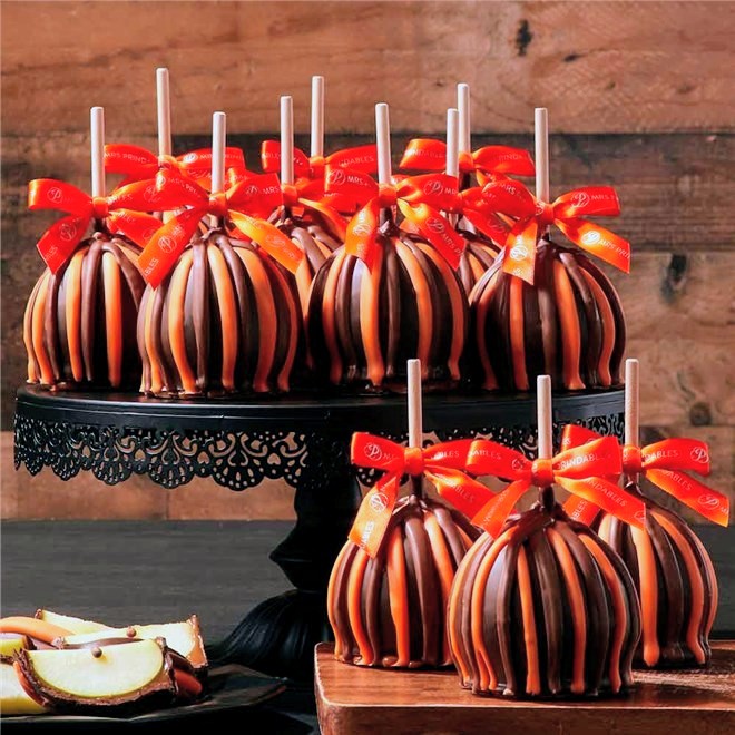Chocolate and caramel striped candy apples with red ribbon bows on wooden tiered stand