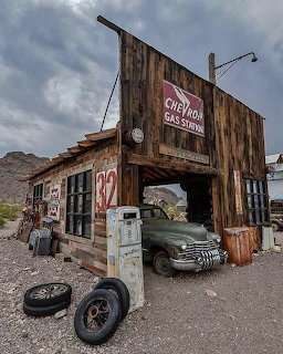 Rustic wooden service station with vintage truck parked under archway, surrounded by old tires in desert setting