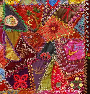 Vibrant patchwork quilt with embroidered flowers, beads, and decorative stitching in red, purple, yellow, and green fabrics