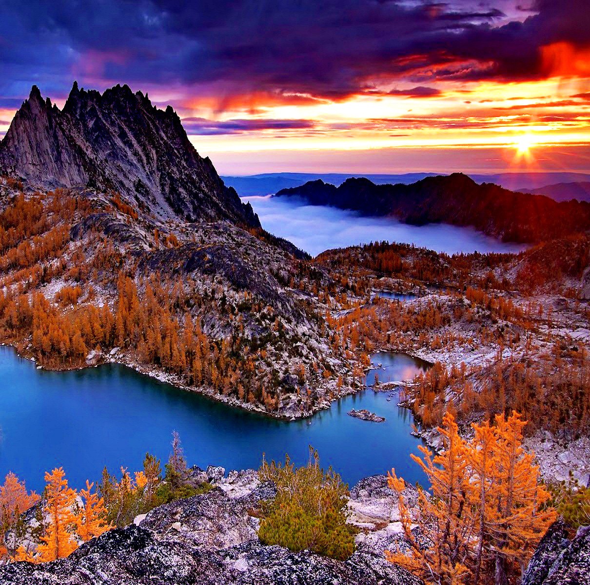 Sunrise over alpine lake with golden larch trees and jagged mountain peaks under colorful sky