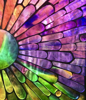 Colorful stained glass artwork with spiral pattern in purple, green, pink and orange hues