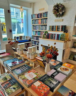 Bright bookstore interior with wooden tables displaying books, shelves lining walls, and decorative wreath