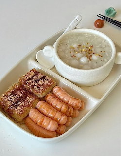 Breakfast tray with bowl of rice porridge, sesame rice cakes, and mini sausages on a white plate
