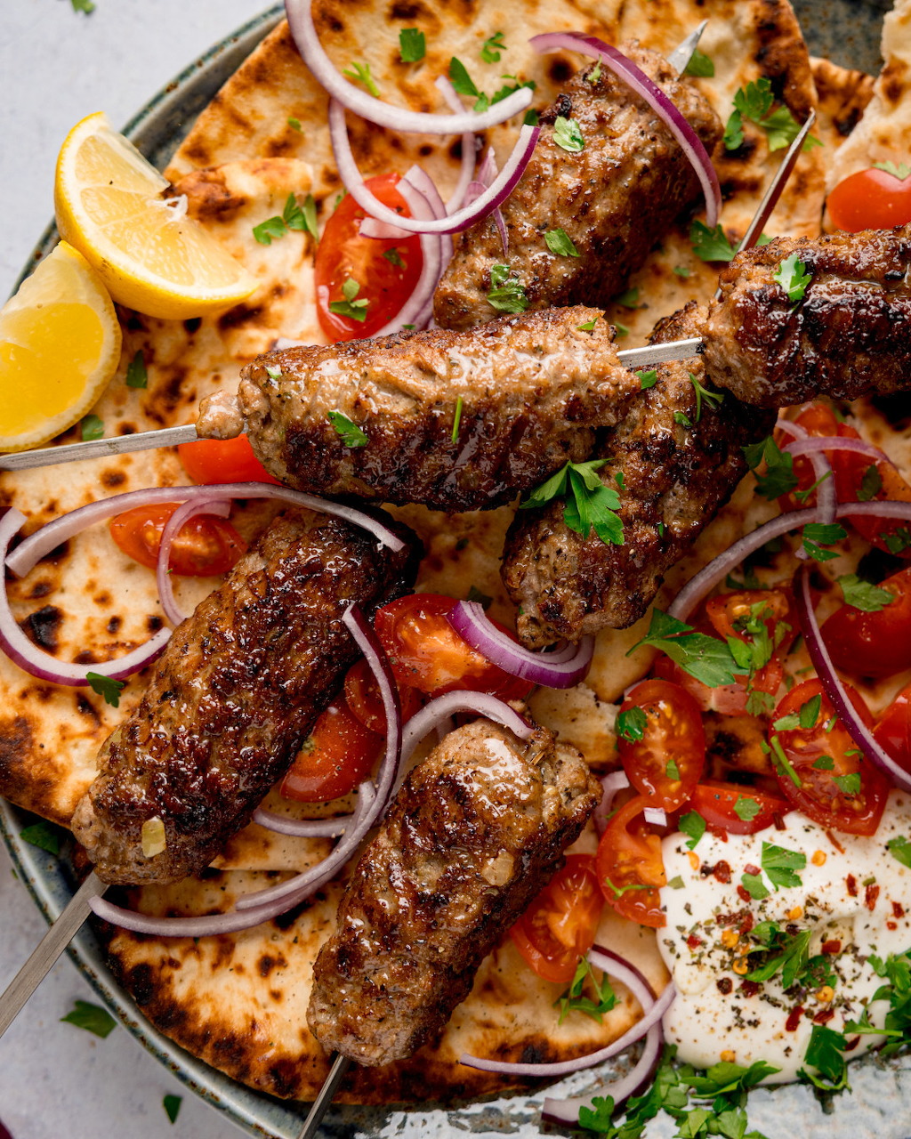 Grilled meat kebabs on flatbread with tomatoes, red onion, parsley, rice, and lemon wedges