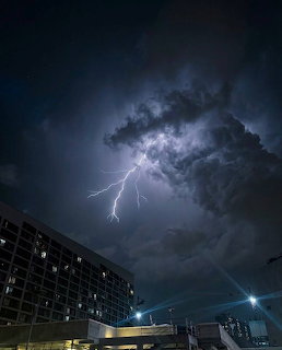Lightning bolt striking from dark storm clouds over city building at night