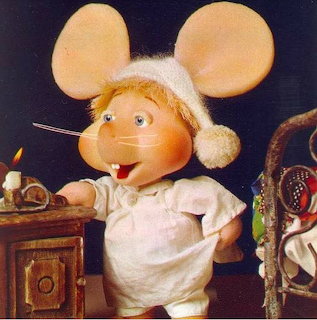 Cartoon mouse doll wearing a Santa hat and white nightshirt beside a candlelit table