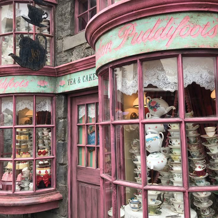 Pink Victorian tea shop storefront with ornate windows displaying teapots and china in a whimsical vintage style