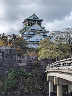 Osaka Castle with multi-tiered architecture, stone walls, and bridge in foreground under cloudy sky