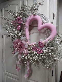 Pink heart-shaped floral wreath with lavender blooms and ribbon hanging on a white door