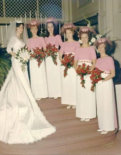 Bride in white wedding dress with five bridesmaids in pink and white dresses holding red bouquets