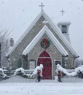 Small stone church with red arched door and Christmas wreath during heavy snowfall