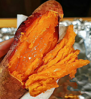 Hand holding a split roasted sweet potato with bright orange caramelized flesh wrapped in foil