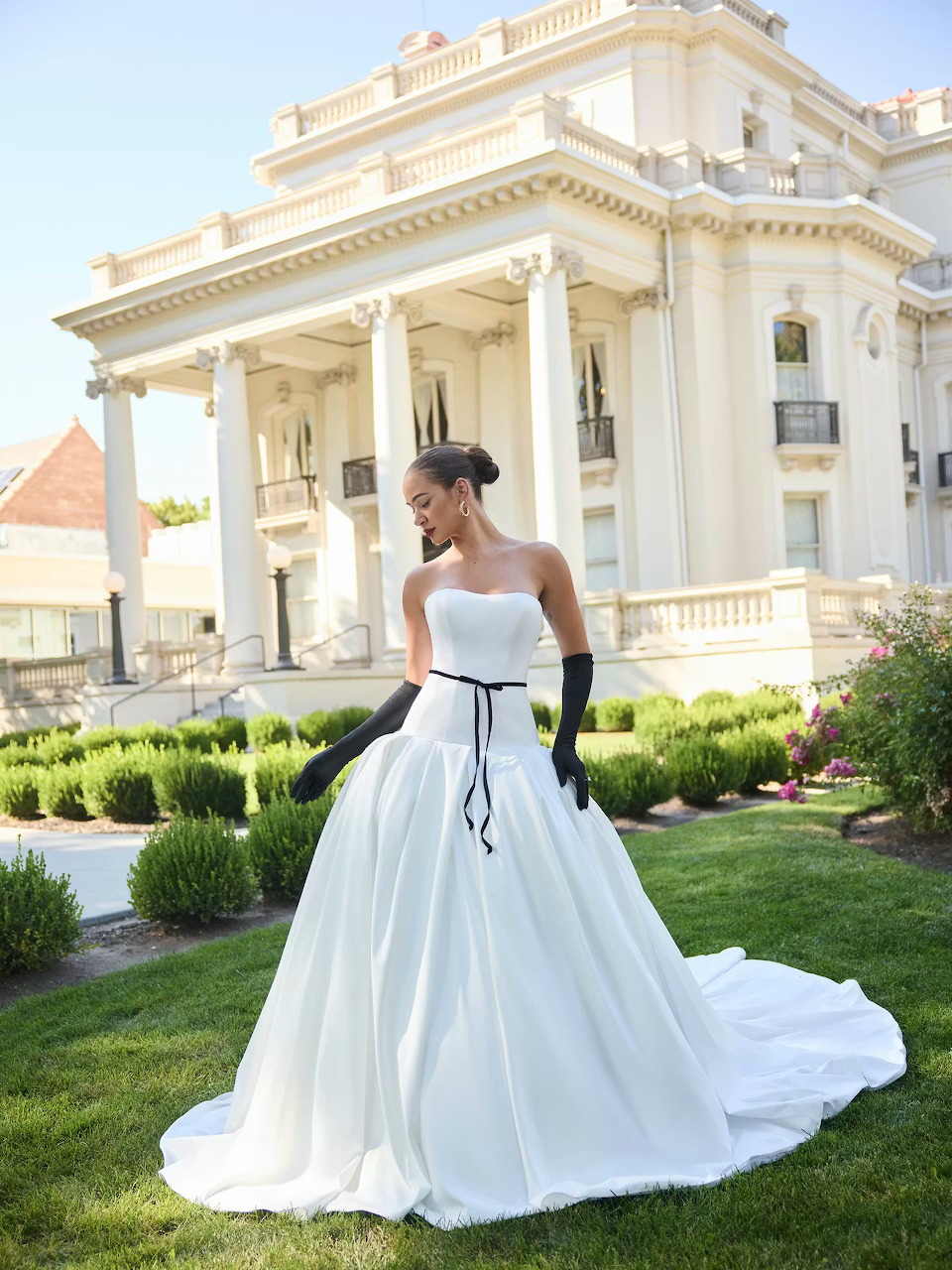 Bride in a white wedding gown standing on a lawn before a grand white building
