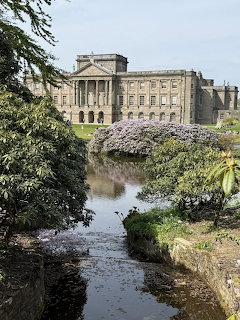 Stone country house across a pond with flowering shrubs and trees