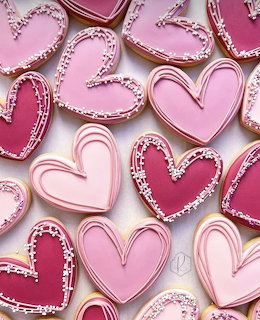 Pink and red heart-shaped cookies with white sprinkle borders arranged on pink surface