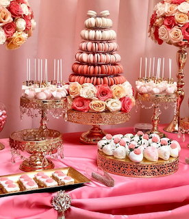 Elegant pink dessert table with macaron tower, roses, cake pops and cupcakes on decorative gold stands