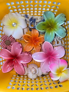 Colorful plumeria flower hair clips in pink, orange, green, and white arranged in a yellow basket