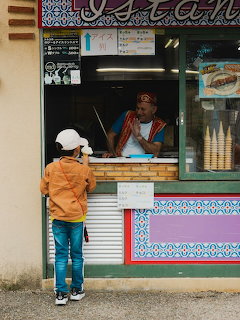 Child at an ice cream stand window with a vendor inside and waffle cones on display