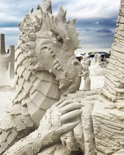 Detailed sand sculpture of a dragon with scales and claws on a beach