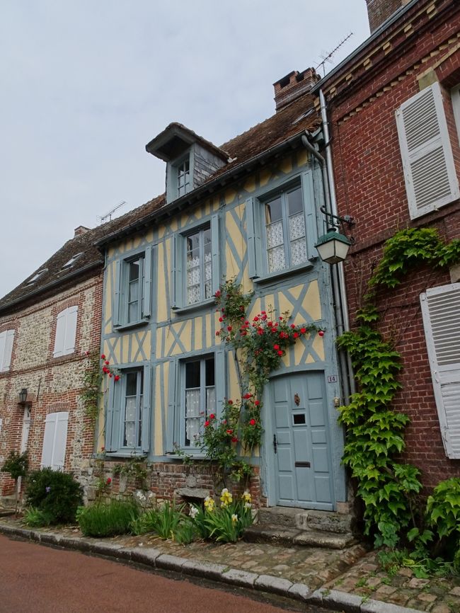Old village houses with blue shutters, flowers, and ivy along a quiet street in Gerberoy, France
