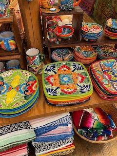 Wooden shelves displaying colorful Mexican ceramic plates, bowls, and pottery with bright floral and geometric designs