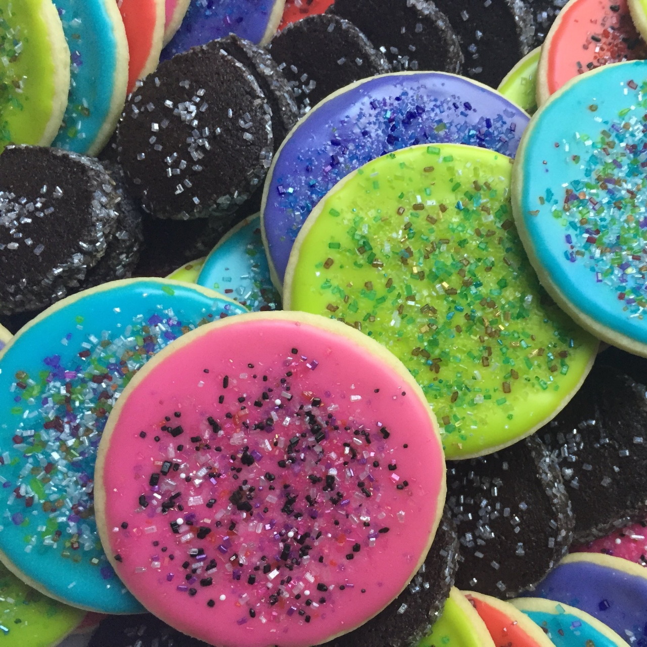Assorted round sugar cookies with bright colored frosting and glitter sprinkles