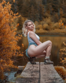 Blonde woman crouching on a wooden dock by a lake surrounded by autumn trees