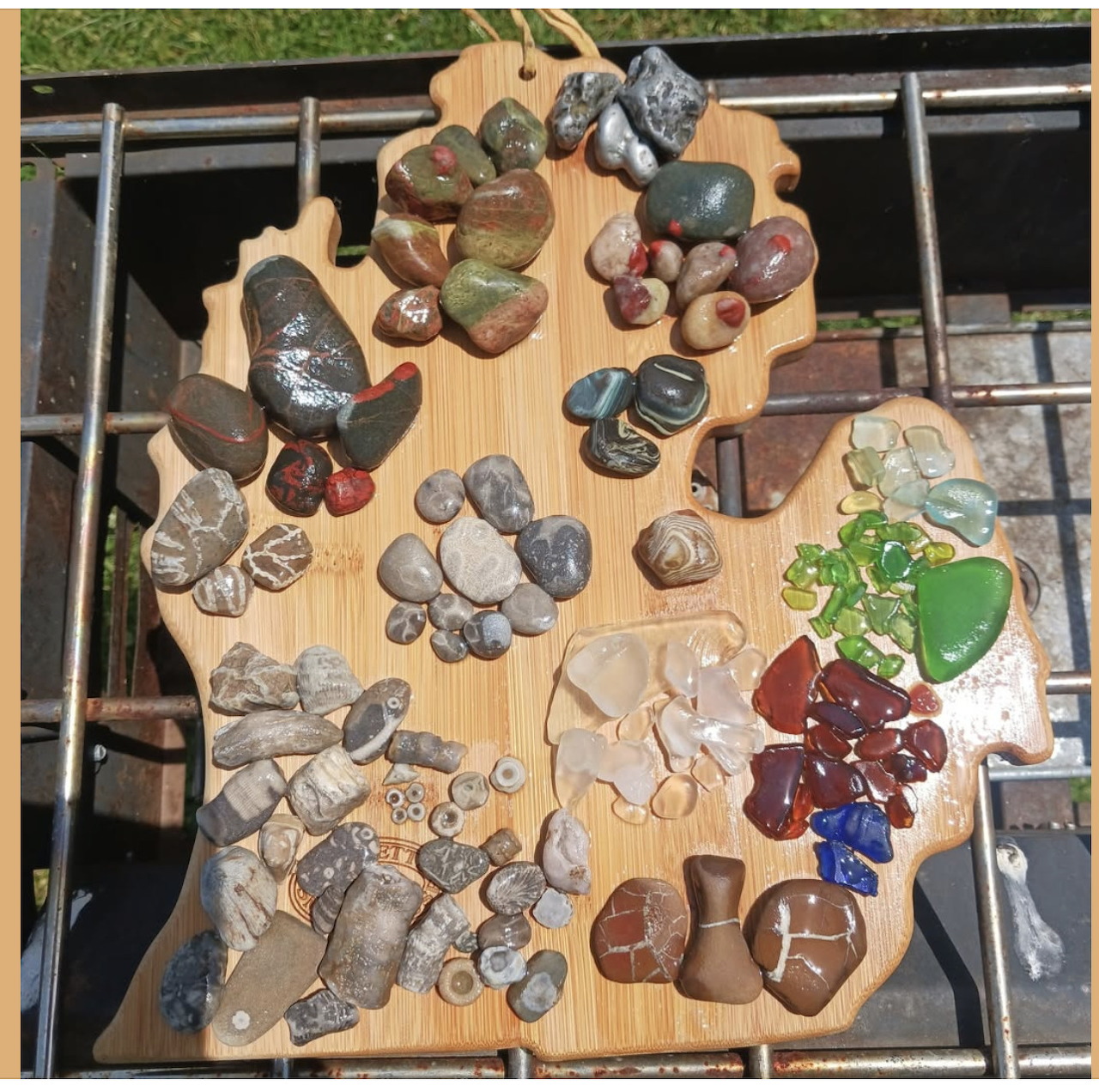 Assorted polished rocks, stones, and sea glass pieces arranged on a Michigan-shaped wooden board