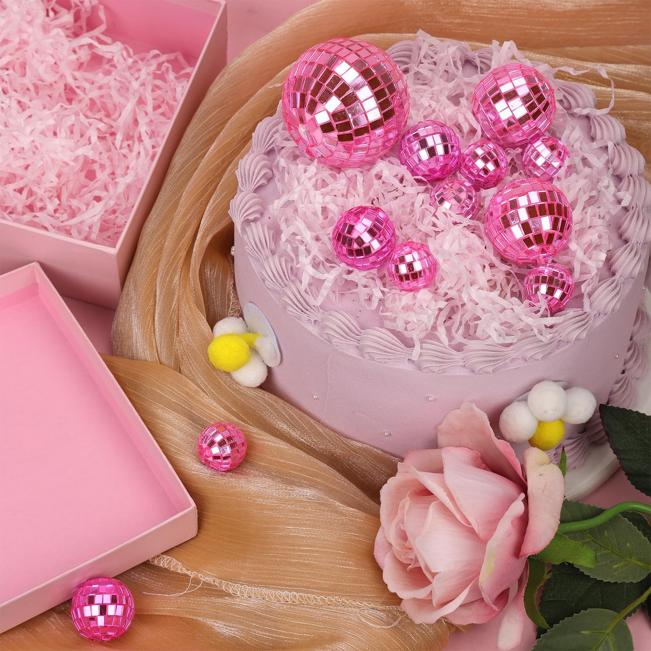 Pink cake with disco ball decorations and rose on wooden board