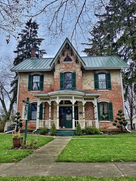 Victorian red brick house with green roof, covered porch, and green lawn on a cloudy day