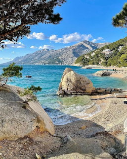 Rocky beach with turquoise sea, large boulders, pine trees, and mountains in Brela, Croatia