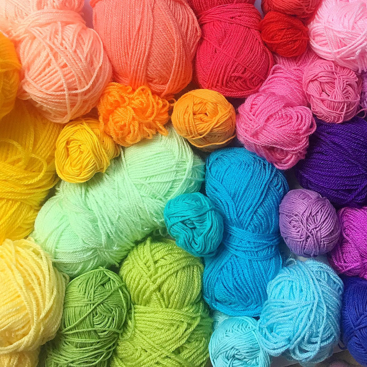 Rainbow arrangement of colorful yarn balls in various shades from orange to purple