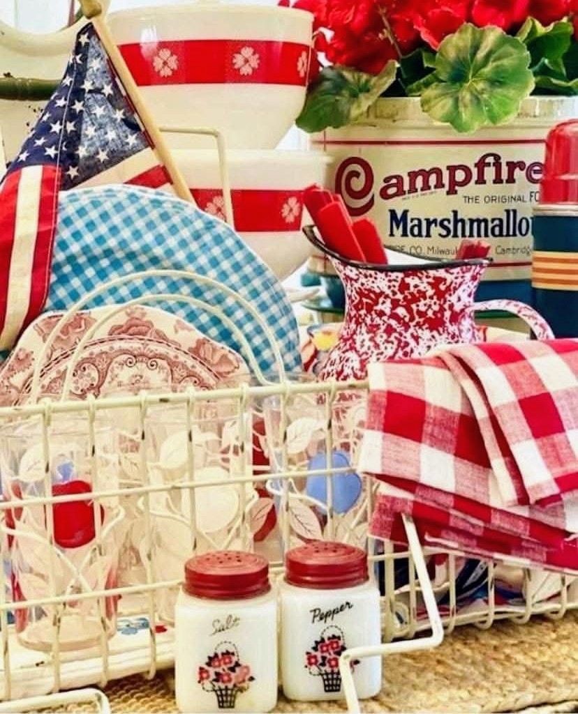 Vintage kitchen display with patriotic plates, checkered cloths, enamel mugs, and marshmallow box
