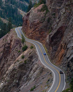 Winding two-lane highway cutting through steep rocky mountain cliffs with a single car on the road