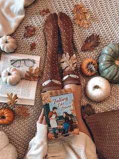 Person in brown polka dot tights holding a book surrounded by pumpkins, autumn leaves, and glasses on a knit blanket