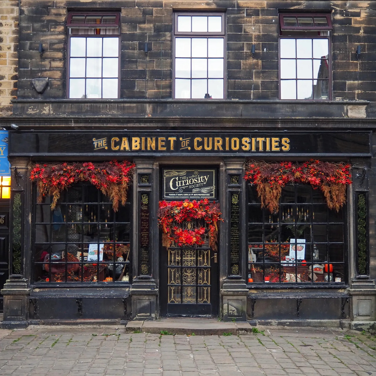 The Cabinet of Curiosities storefront with black facade, large windows, and red flowers