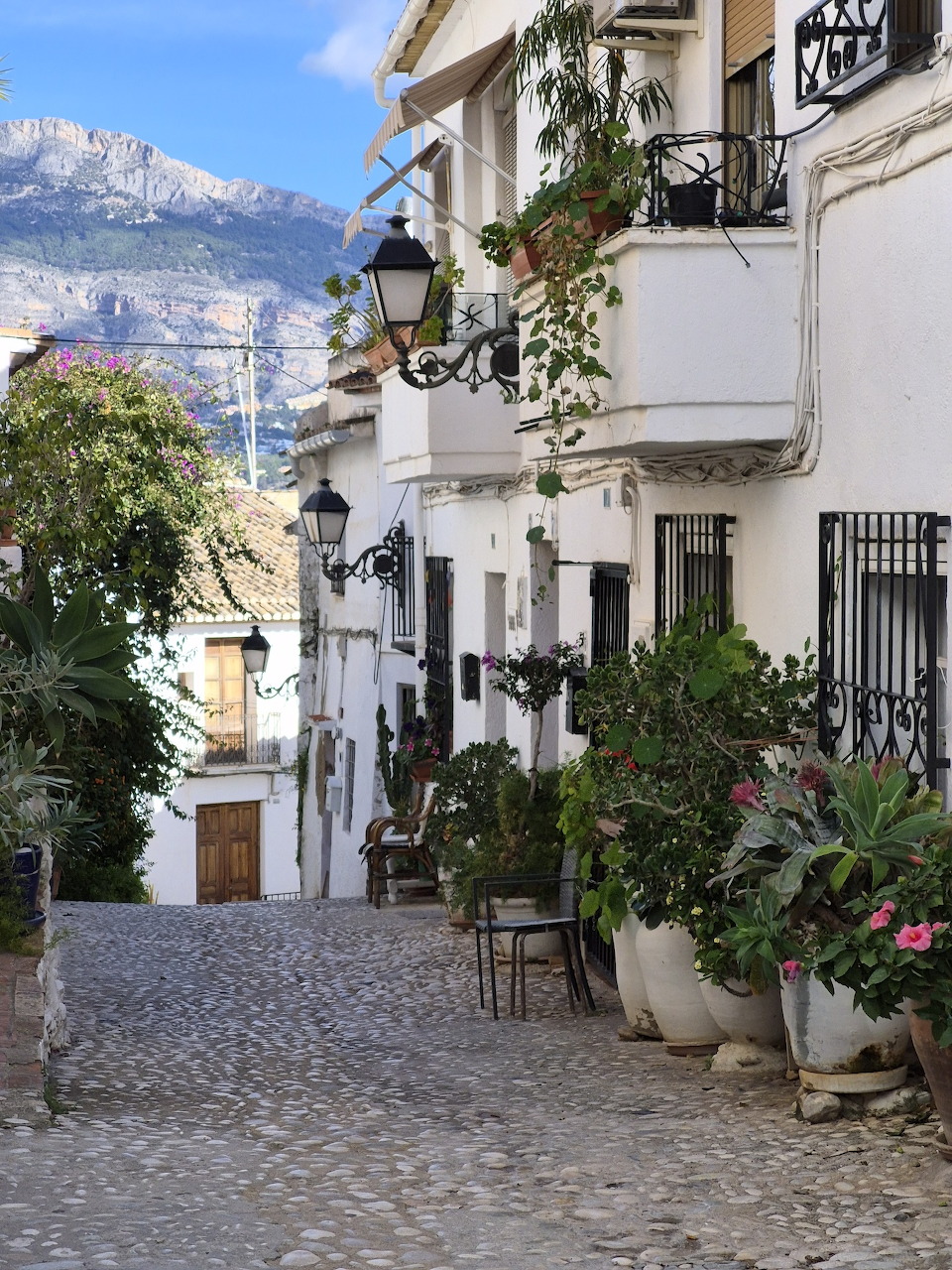 Narrow cobblestone street lined with white buildings and potted plants in Altea, Spain