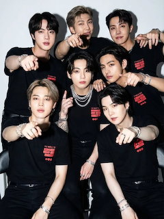 Seven young men in matching black t-shirts posing together for a group photo against a gray background