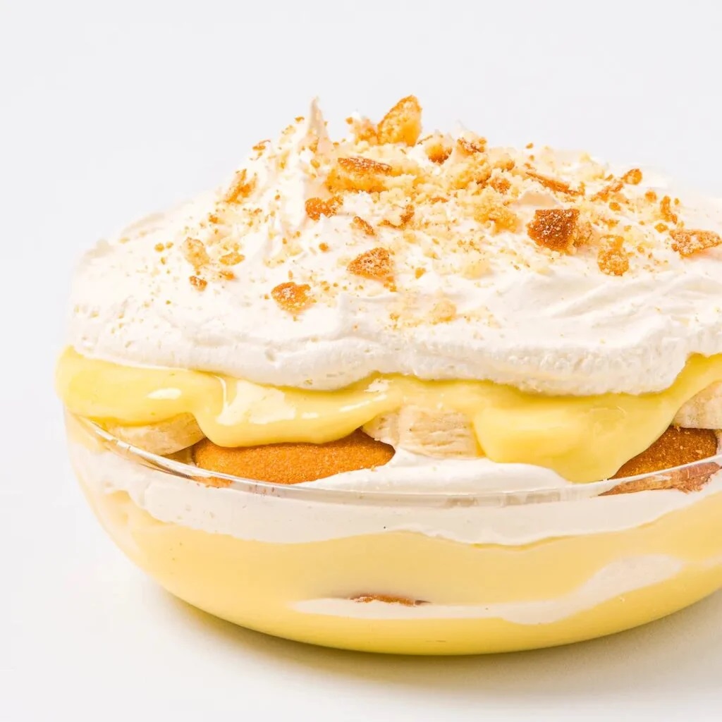 Layered banana pudding with whipped cream, vanilla wafers, and banana slices in a clear glass bowl