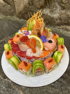 Decorative sushi cake with salmon, shrimp, cucumber, roe, and lemon on a white plate