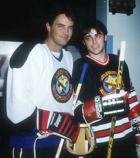 Two men wearing hockey jerseys standing together indoors, smiling at camera in 1990s photograph