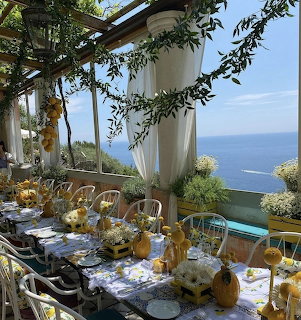 Decorated seaside dining table with flowers, white chairs, and ocean view through open windows